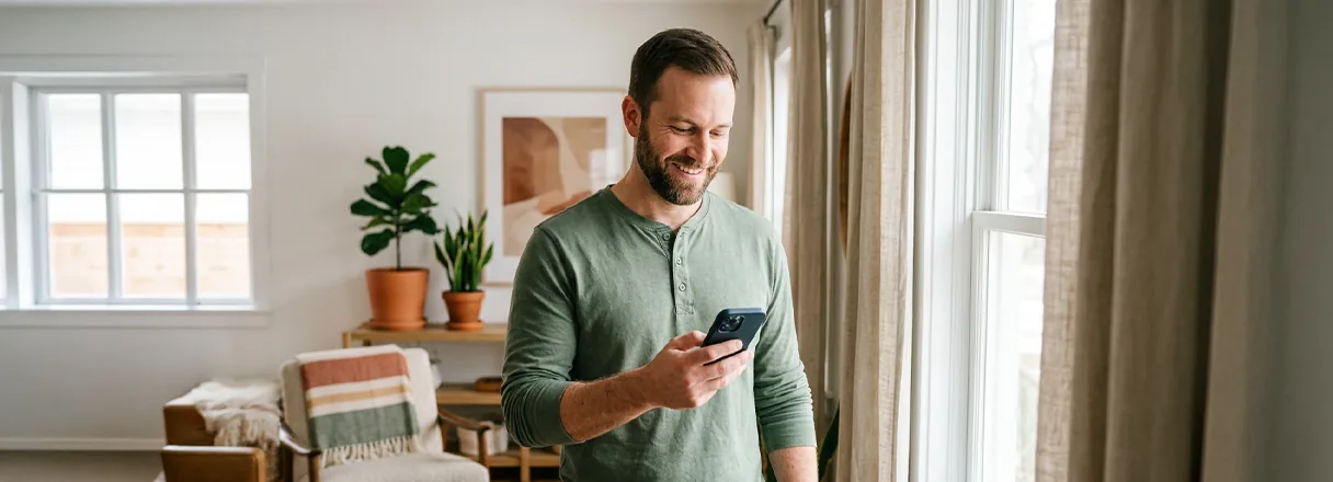 A man by a bright window checking loan offers on his phone